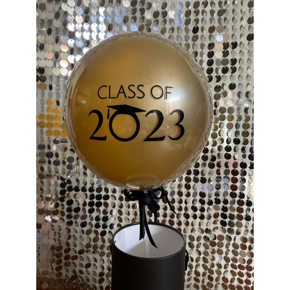 Gold balloon in black much with black tie. Class of 2023 written in black on the balloon